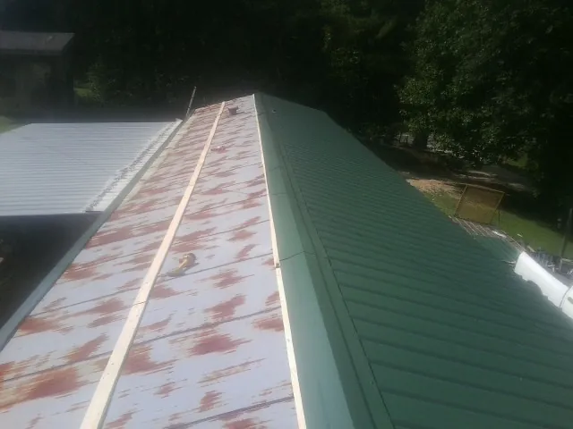 Old rusted panels beside newly installed green metal roofing — Wind Damage Roof Repair by Roofing Brothers in Chapmansboro