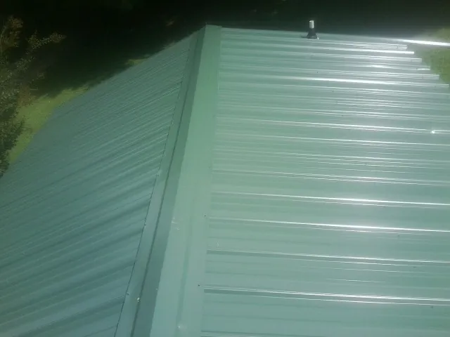 New green metal panels meeting at the ridge of a roof — Flat Roof Repair work by our crew in Chapmansboro