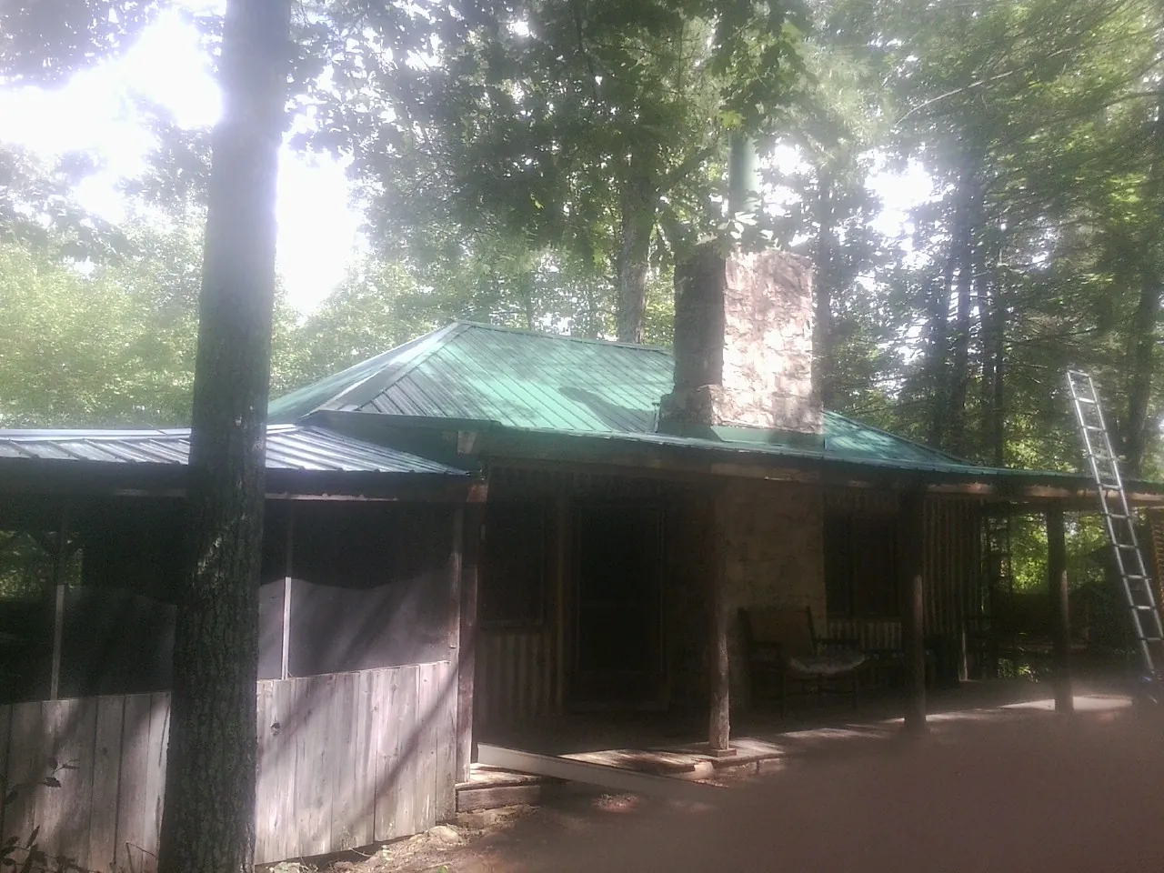 Green metal roof and stone chimney above a log cabin porch in Chapmansboro