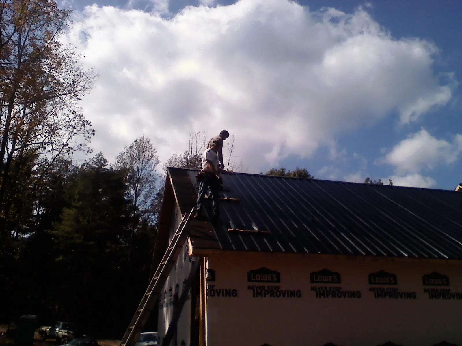 Roofer fastening dark metal panels high against a cloudy sky, from a Roof Inspection job in Chapmansboro