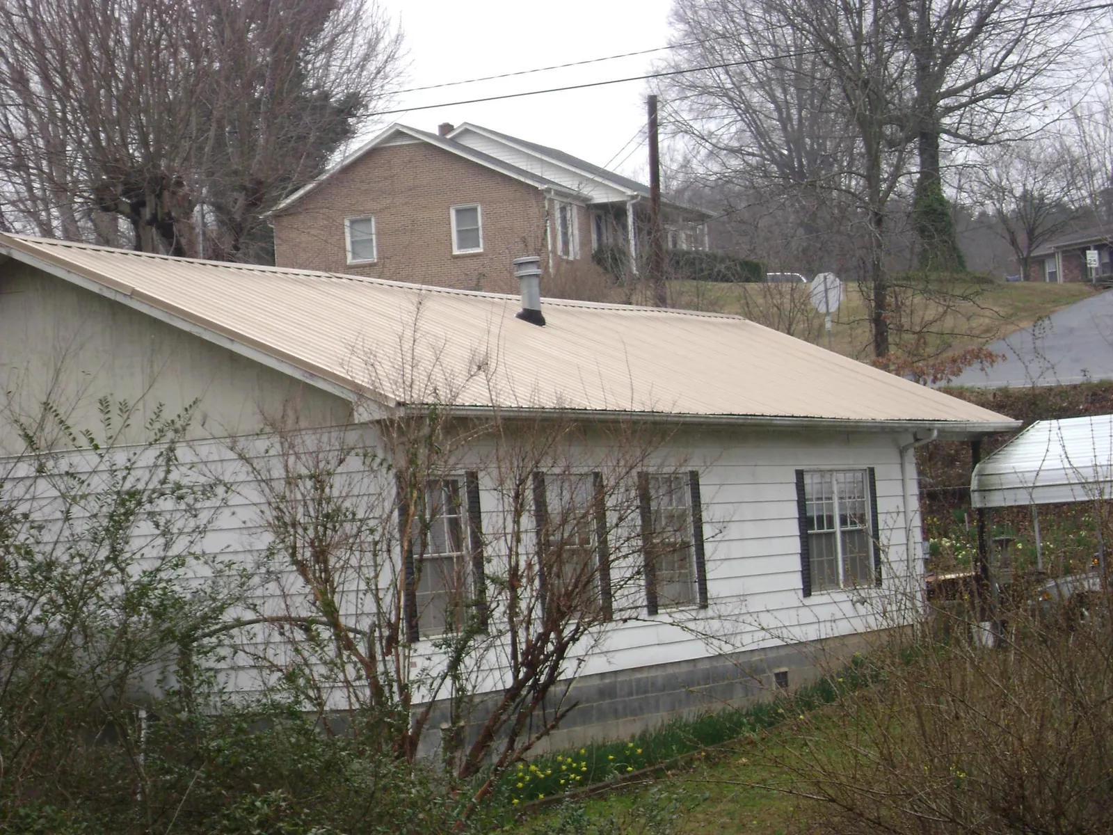 Tan metal roof on a white sided house set into a hillside — Commercial Roofing by Roofing Brothers in Chapmansboro