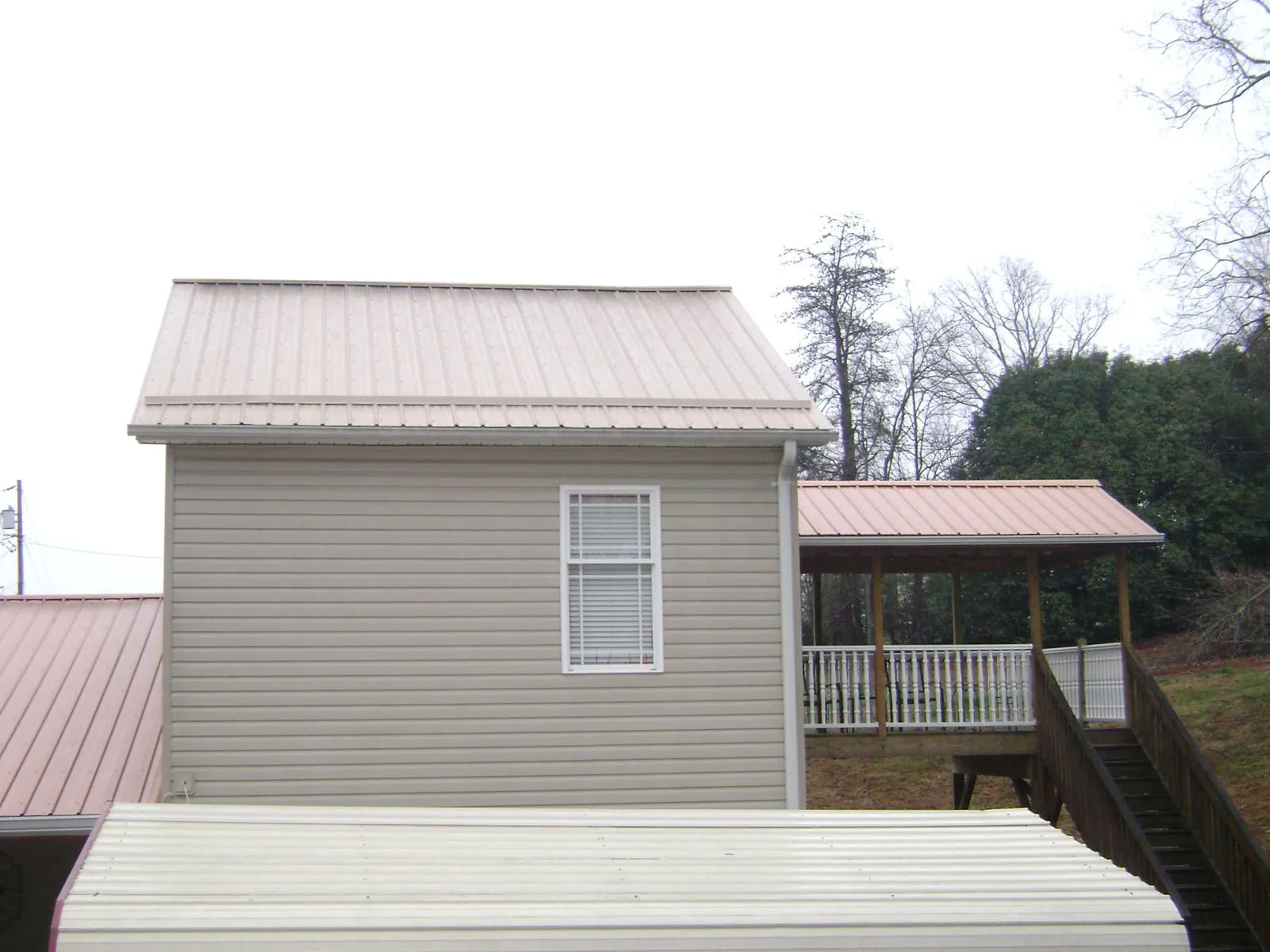 Tan metal roofs on a two story addition and attached porch, from a Roof Replacement job in Chapmansboro